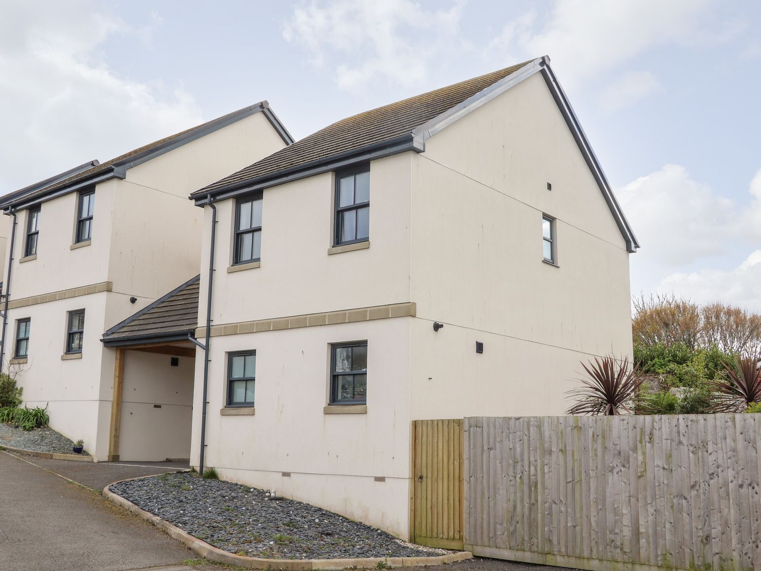 A detached house with beige walls and black framed windows next to a wooden fence at 1 Queensway Gardens in Hayle