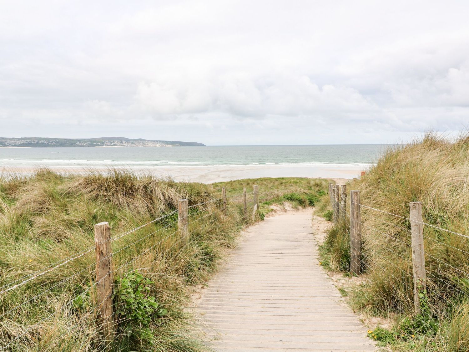 A sandy pathway between grass dunes leading to the beach with the ocean in the background at 1 Queensway Gardens in Hayle