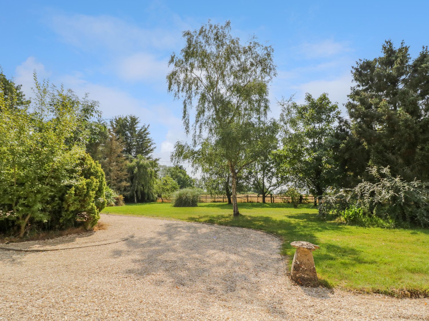 A garden with gravel driveway and various trees under a blue sky at The Paddock in New Yatt near Witney