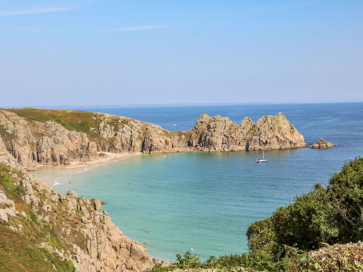 A rocky coastline with a sandy beach and a boat on the water at Beachcomber in Porthcurno near Sennen