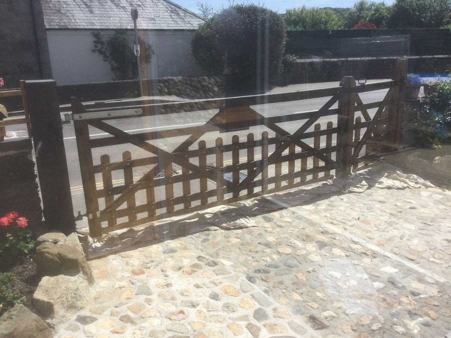 A wooden gate with a cobblestone driveway and a road beyond at Woodbine Cottage in Mylor Bridge Nr Falmouth