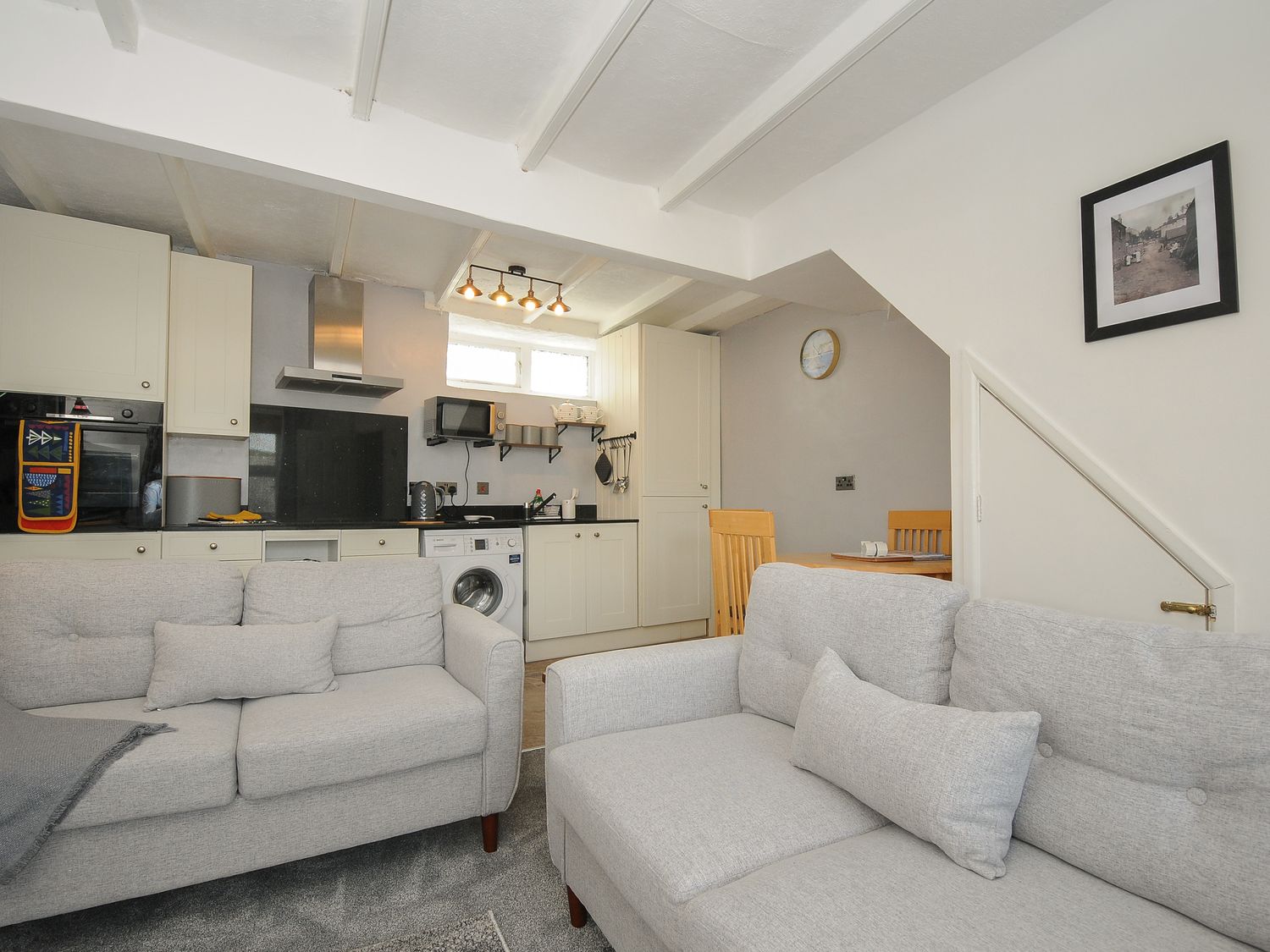 A room with two grey sofas facing a kitchen area with white cabinets a washing machine and a dining table with chairs