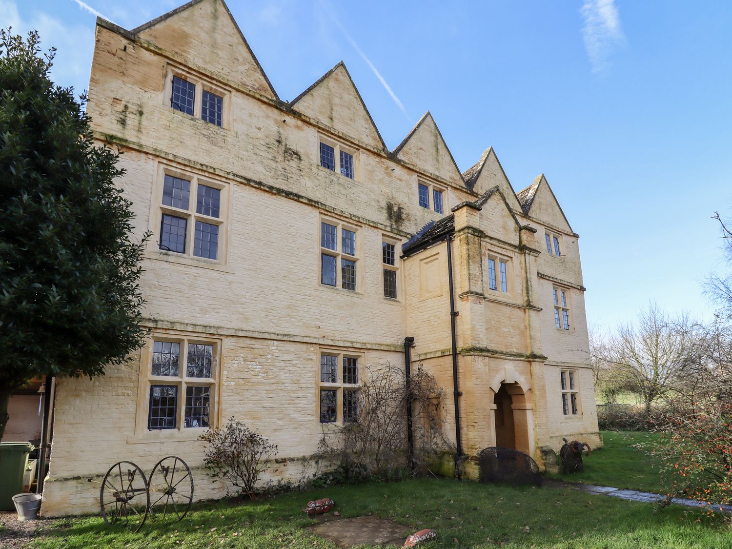 The exterior of a stone building with multiple windows and gabled roofs surrounded by grass and trees at Wick Court Farm in Arlingham near Frampton On Severn