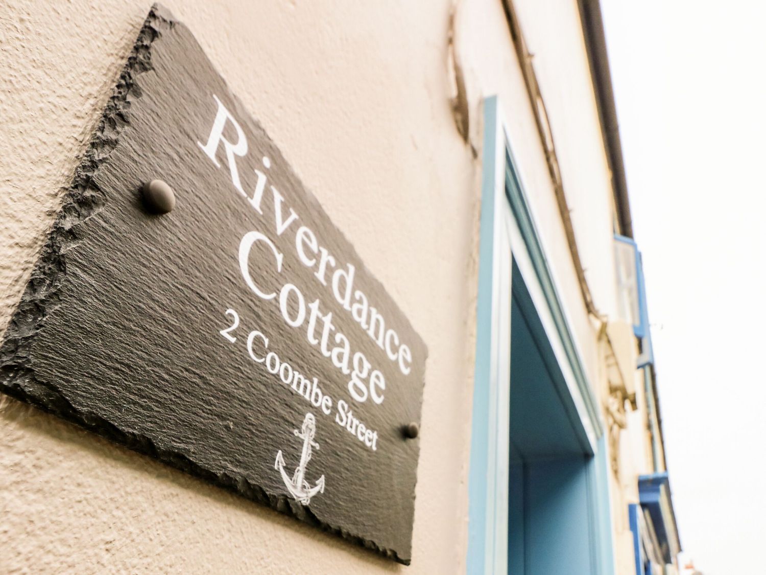 A slate sign reading Riverdance Cottage 2 Coombe Street mounted on a building wall near a blue doorway at Riverdance Cottage in Lyme Regis
