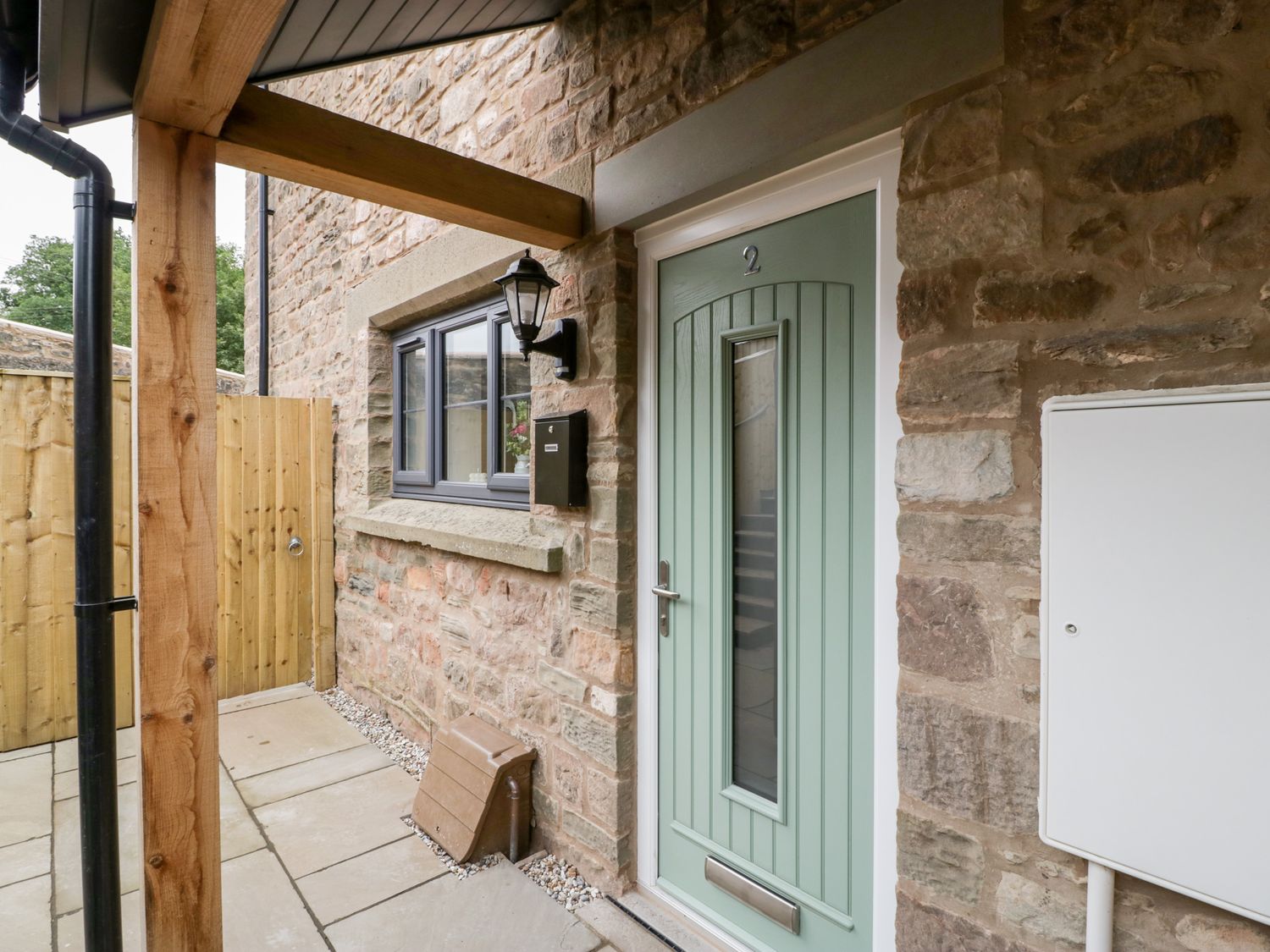 A green front door with a window and number 2 on a stone wall with a window and wooden gate at 2 The Old School in Ruspidge
