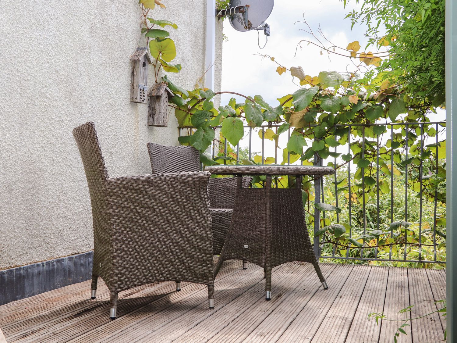 An outdoor balcony with two wicker chairs and a wicker table with climbing plants on the railing at Sea View in St Austell