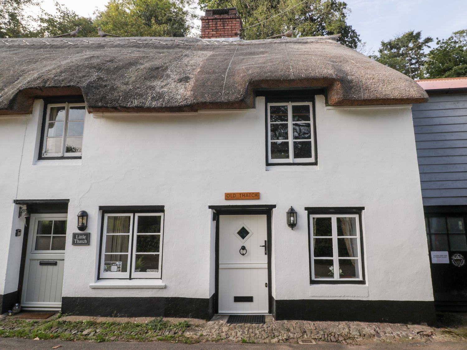 A white thatched cottage with black trim around windows and doors at The Old Thatch in Porlock