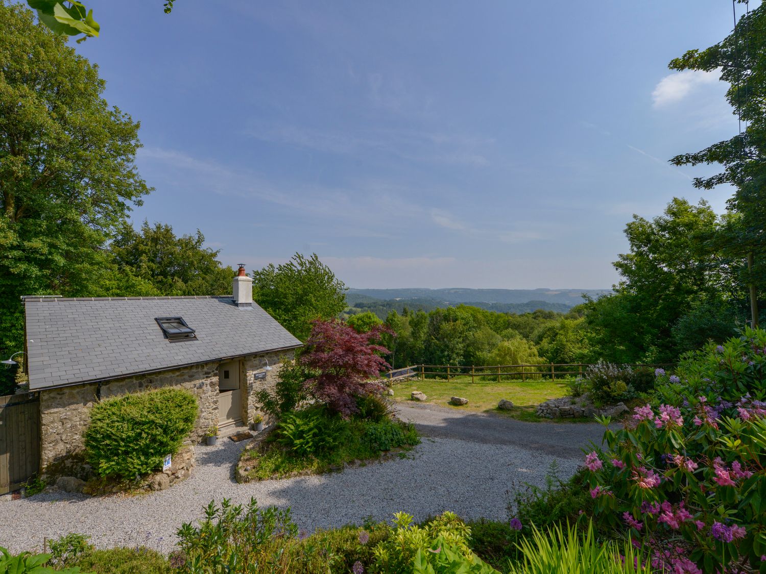 A small stone cottage with a gravel driveway surrounded by trees and flowers at Beckaford View in Manaton near Ilsington