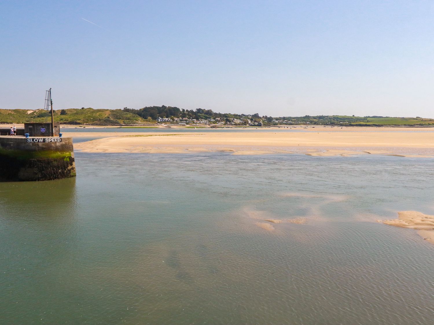 A coastal scene with a water channel a sandy shore a grassy hill and houses in the distance at Piran Lodge in Padstow