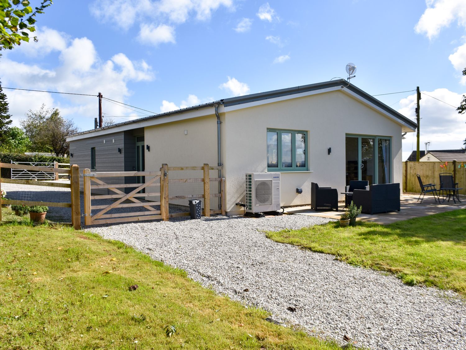 A single story house with a gravel driveway a wooden gate garden furniture and a lawn at The Linhay in Lapford