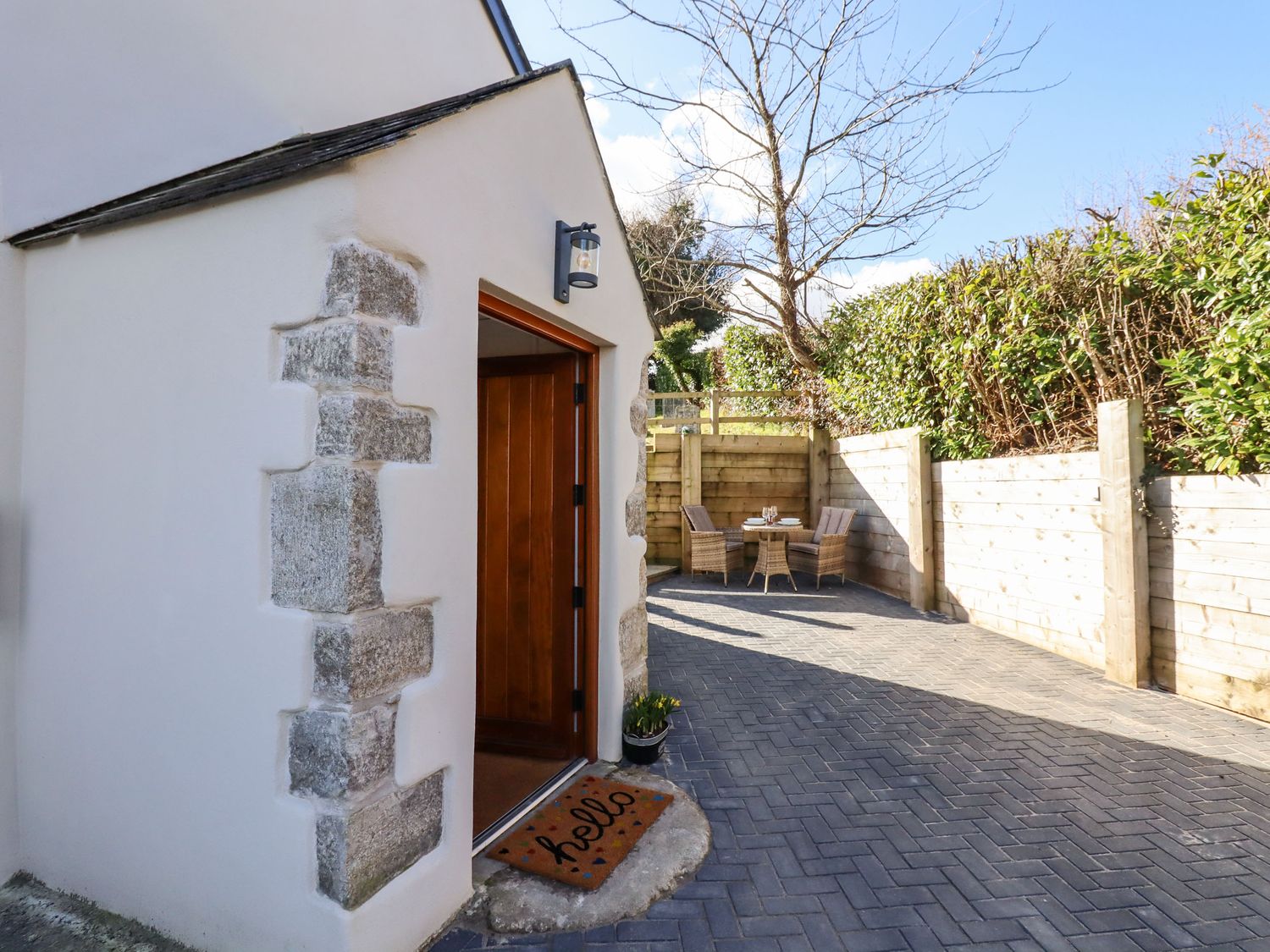 A patio area with a wooden door open and a welcome mat beside a table with chairs at The Old Chapel in Ilsington