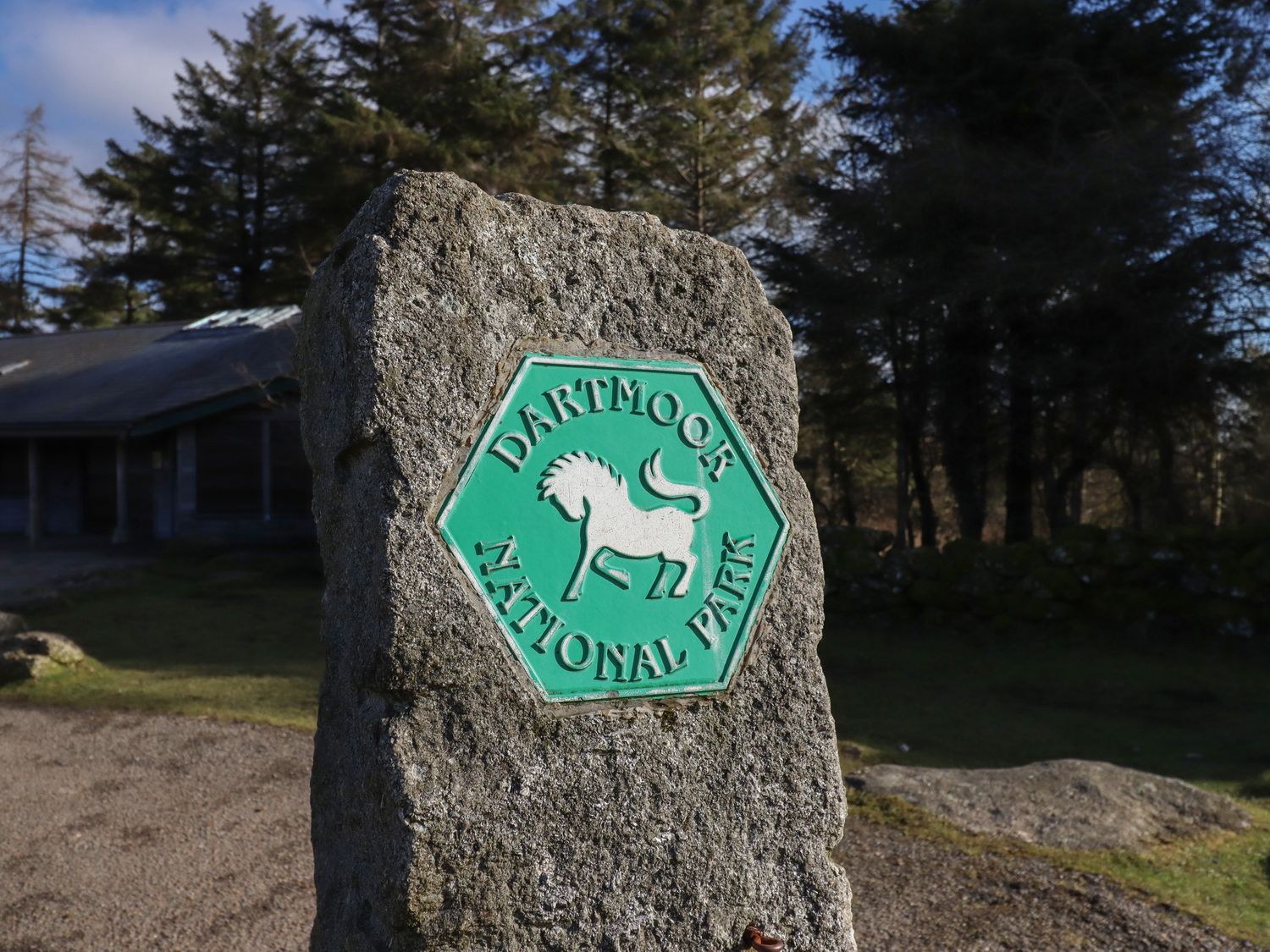 A stone pillar with a Dartmoor National Park sign in a wooded outdoor area at The Old Chapel in Ilsington