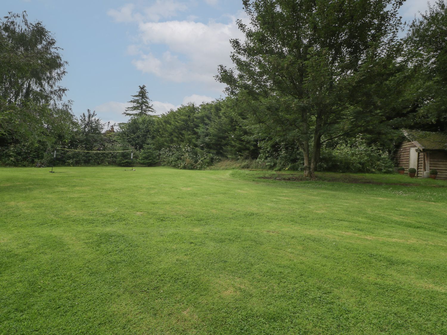 A grassy garden with a badminton net a tree and a wooden shed at Owl Barn in Marston Stannett near Leominster