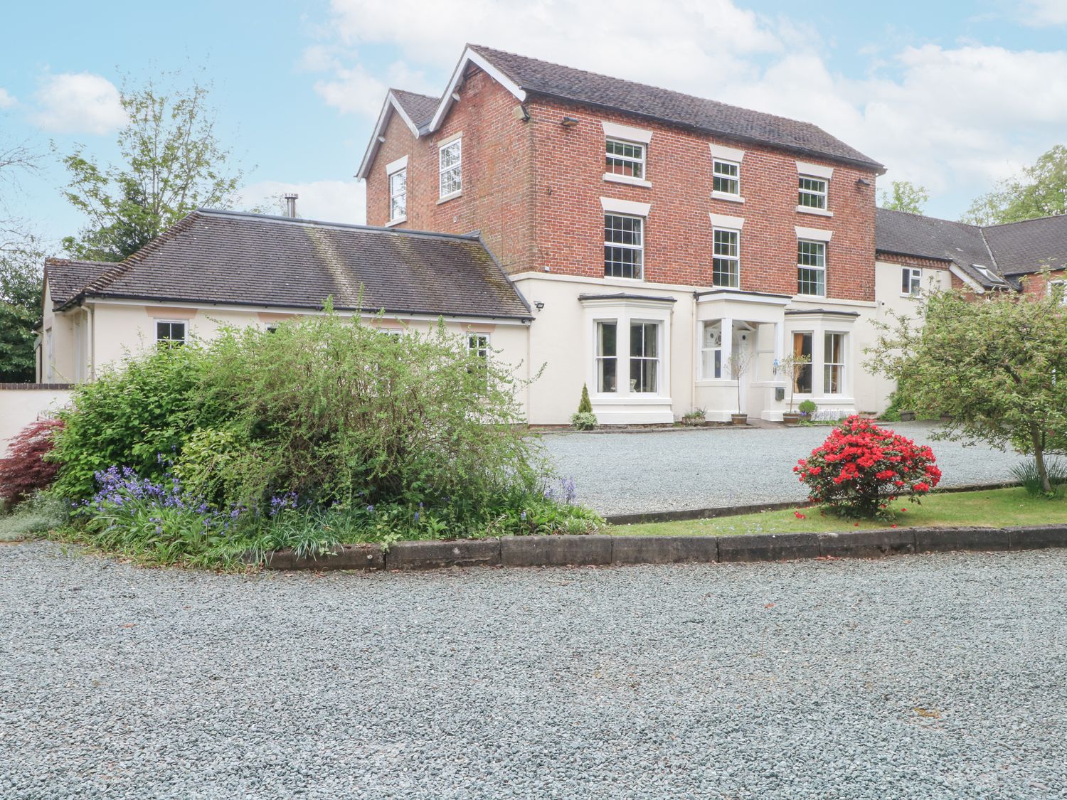 A large brick and white house with gravel driveway and garden shrubs at Rosehill Manor in Rosehill near Market Drayton