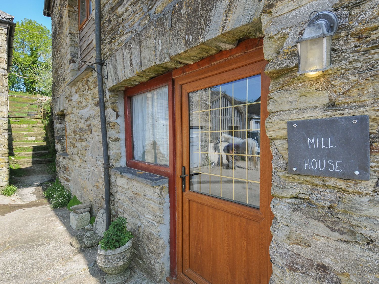 Stone wall with wooden door and window with stairs and greenery outside at Mill House Lostwithiel near Pelynt