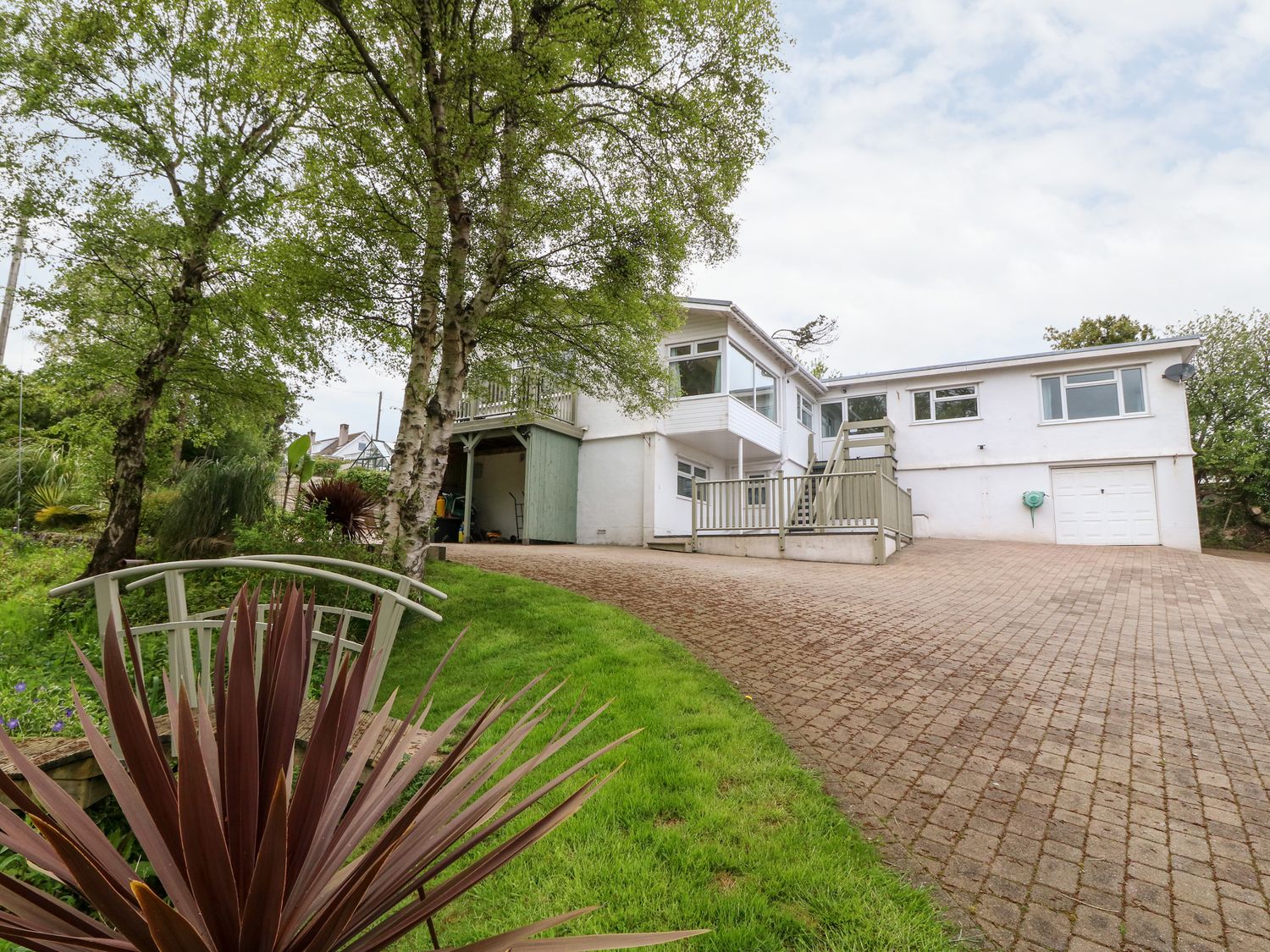 A white house with a paved driveway and surrounding trees and plants at Willoway in Benllech