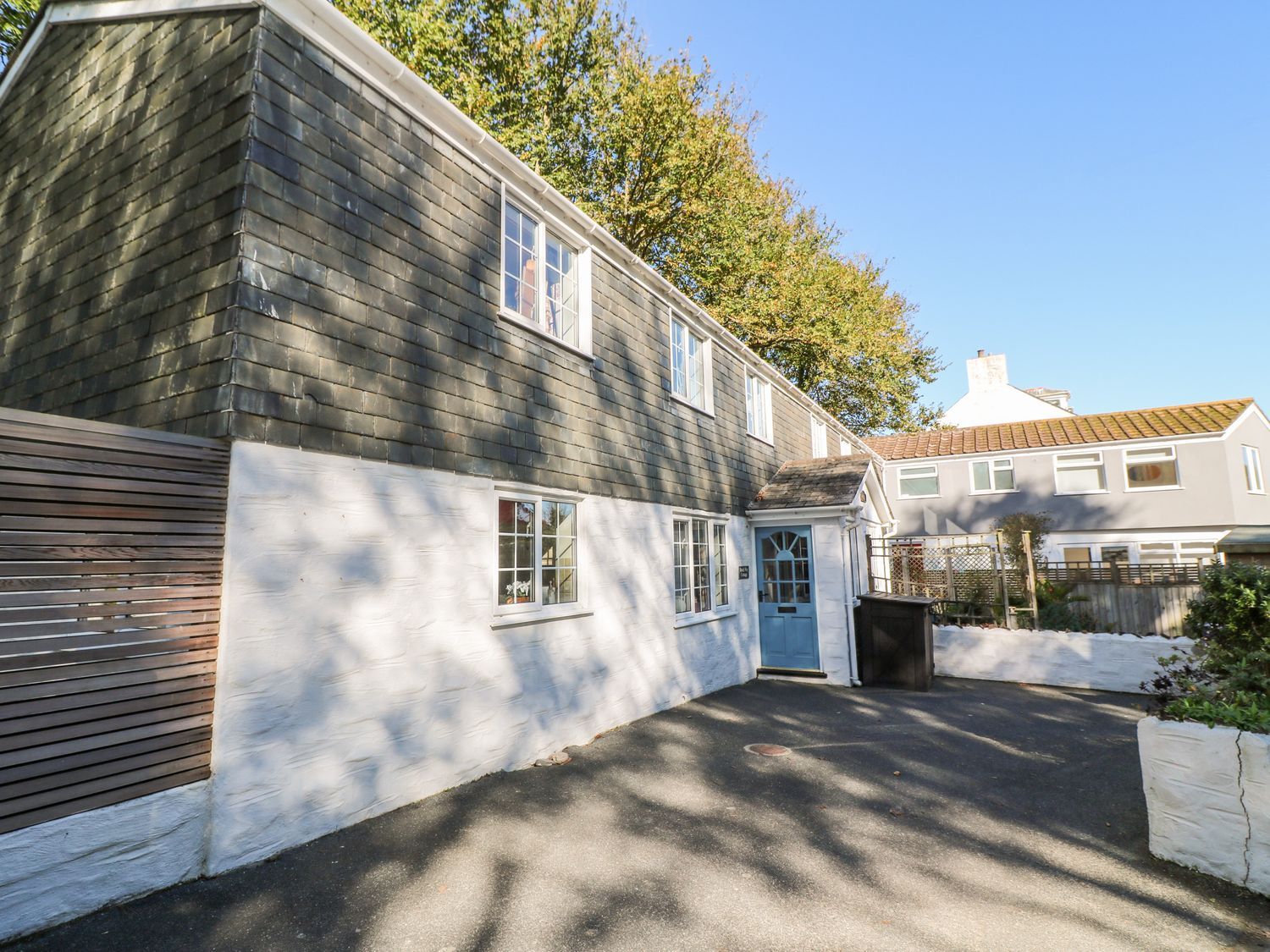 Exterior of a two-story house with grey shingles on the upper floor and white walls on the lower floor at Beach Way Cottage in Gorran Haven