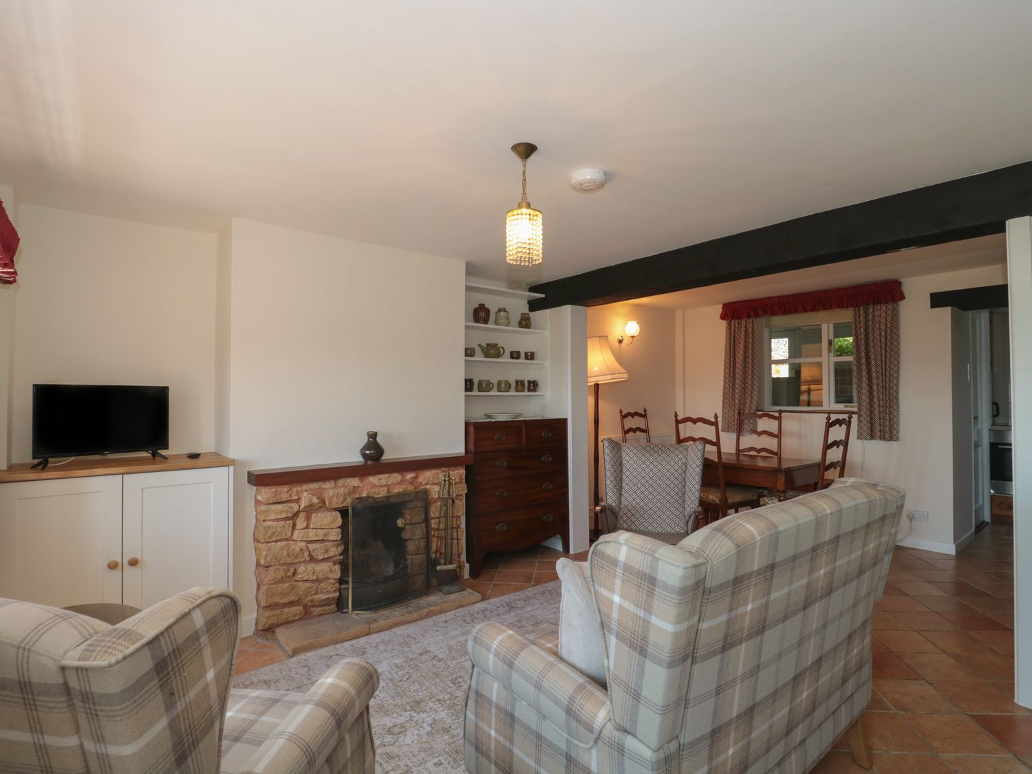 A living room with plaid armchairs a fireplace a television a chest of drawers and a dining table with chairs at Stonecutter's Cottage in Stoke-Sub-Hamdon Somerset
