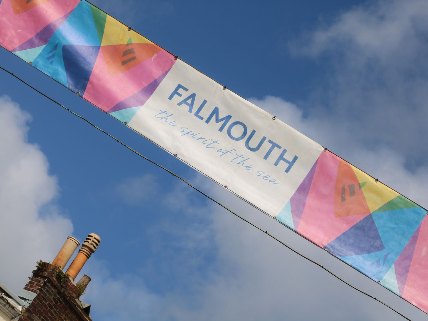 A colorful banner with the text Falmouth the spirit of the sea hanging against a blue sky with clouds