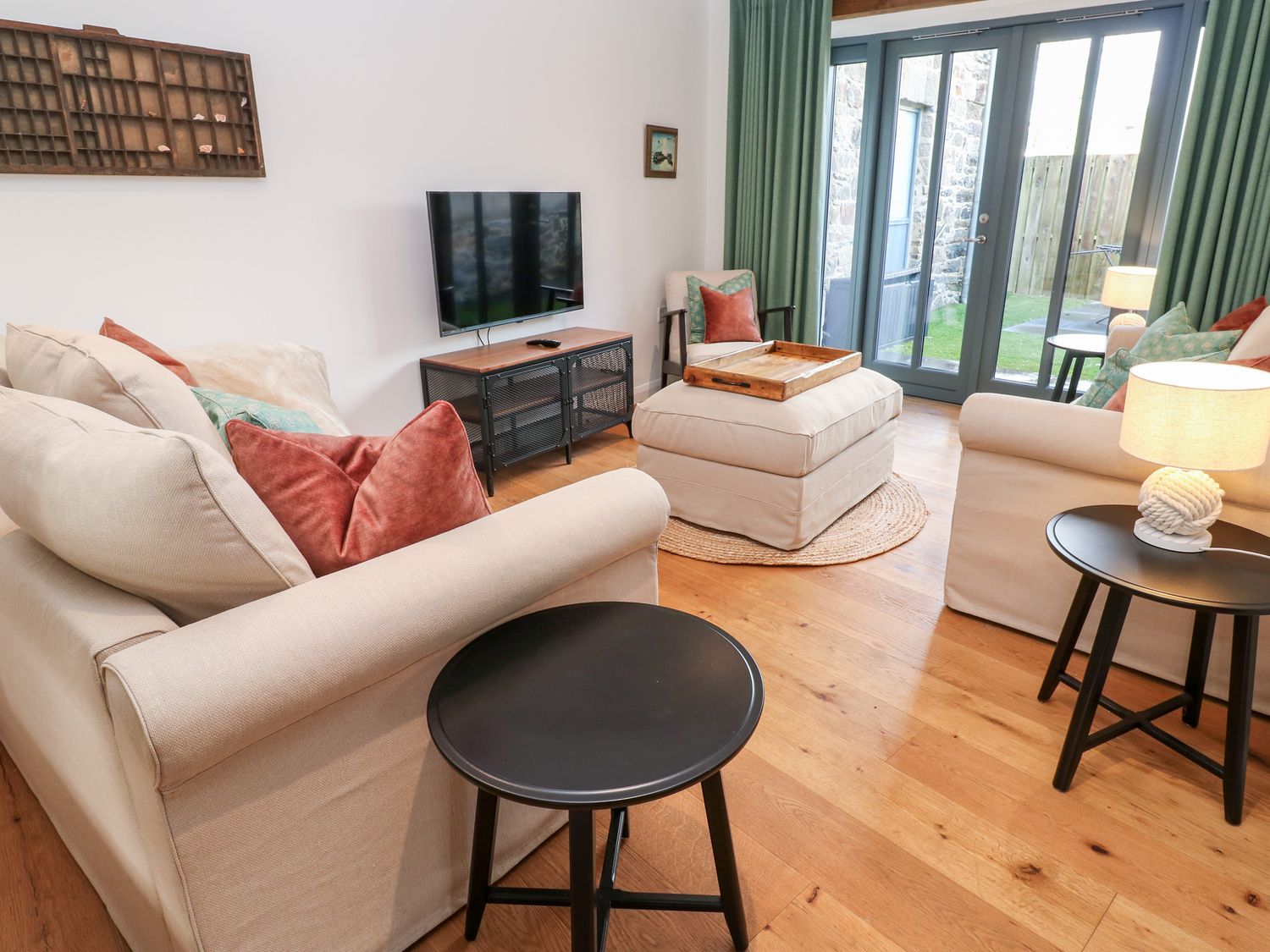 A living room with beige sofas green curtains a television on a stand and wooden flooring at Carines Barns - Pen in Cubert