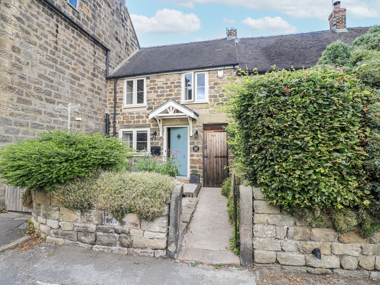 A house with a front door and windows surrounded by bushes at Clematis Cottage in Fritchley near Crich