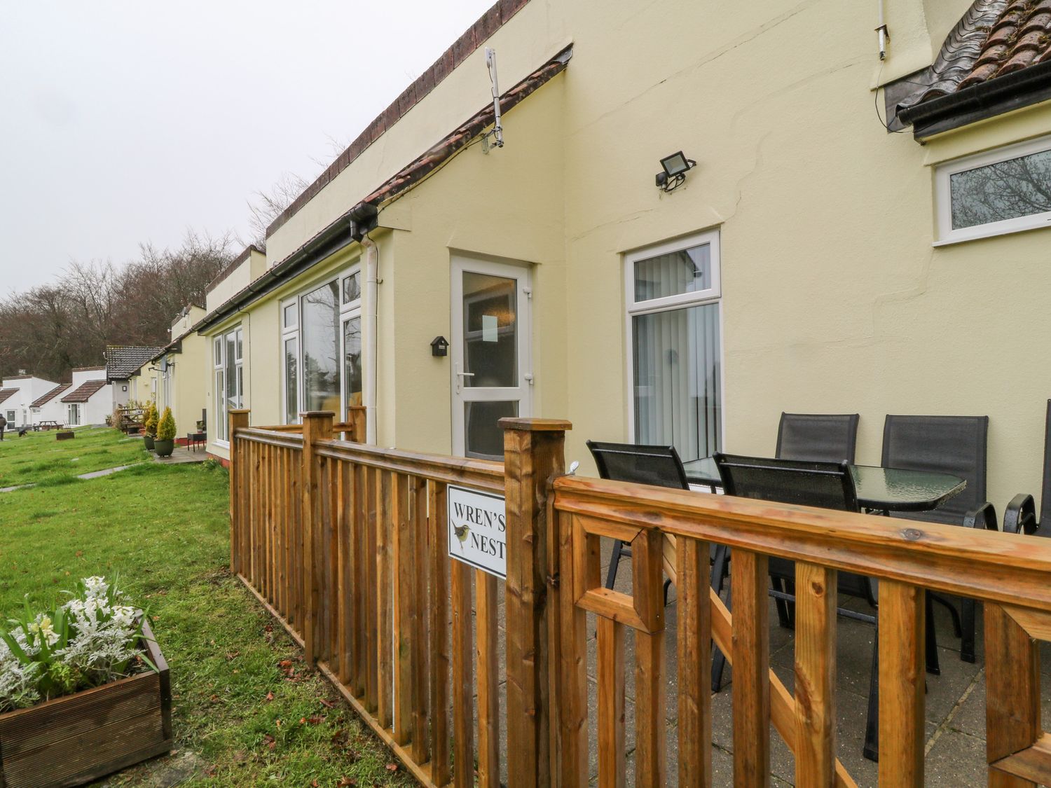 A row of single-story houses with yellow walls and patio areas with tables and chairs at Wren's Nest Manorcombe in Honicombe Park near Gunnislake