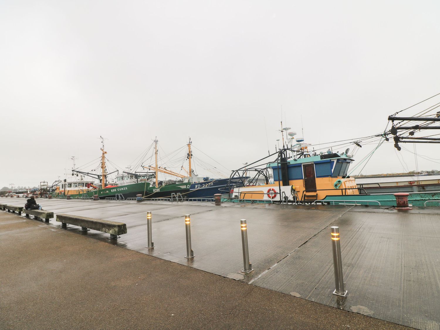 A dock with fishing boats moored along the pier and a person sitting on a wooden bench at 78 King Street in Waberthwaite