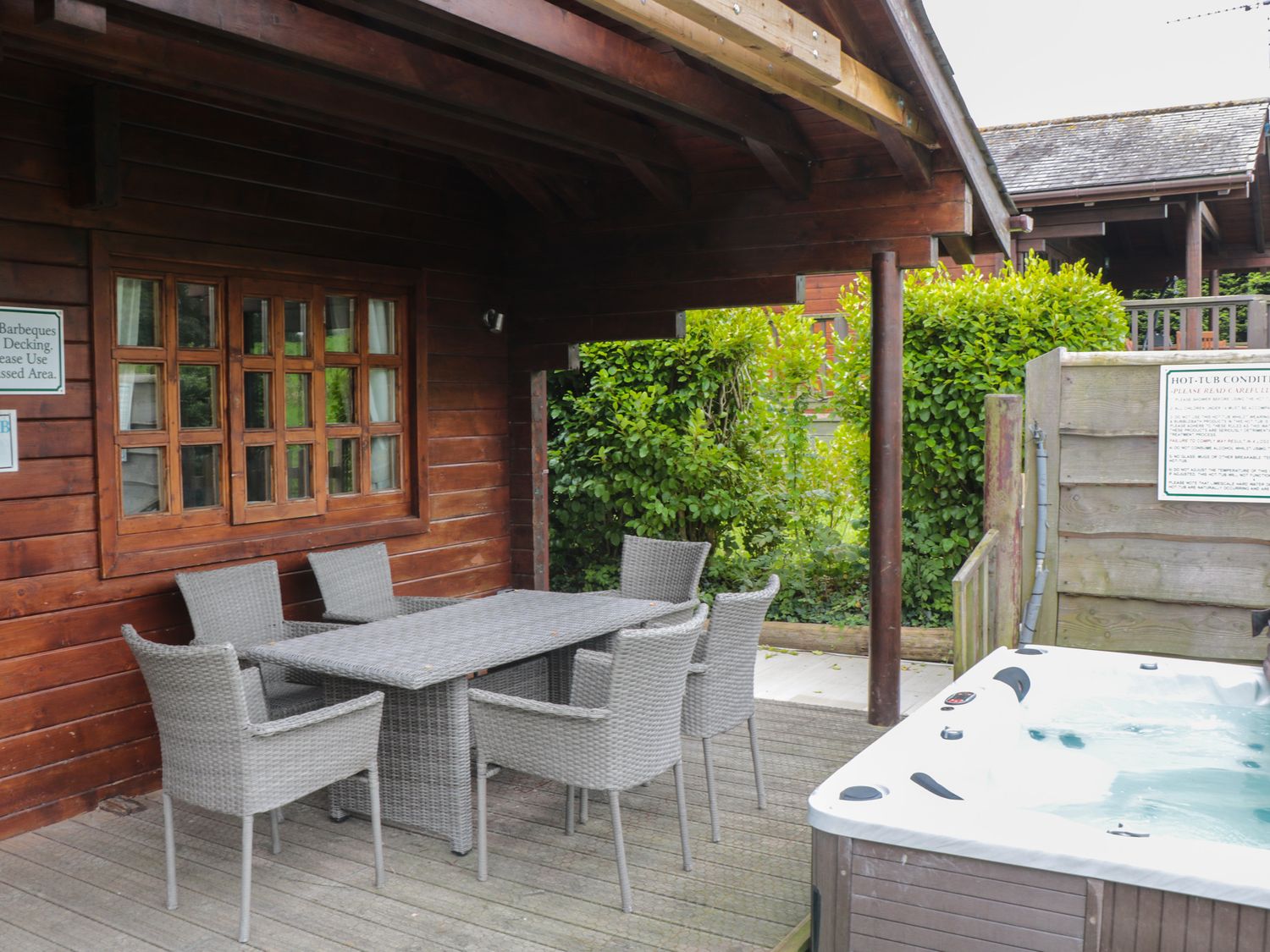An outdoor covered seating area with a table and six chairs next to a hot tub at Pine in Swanage