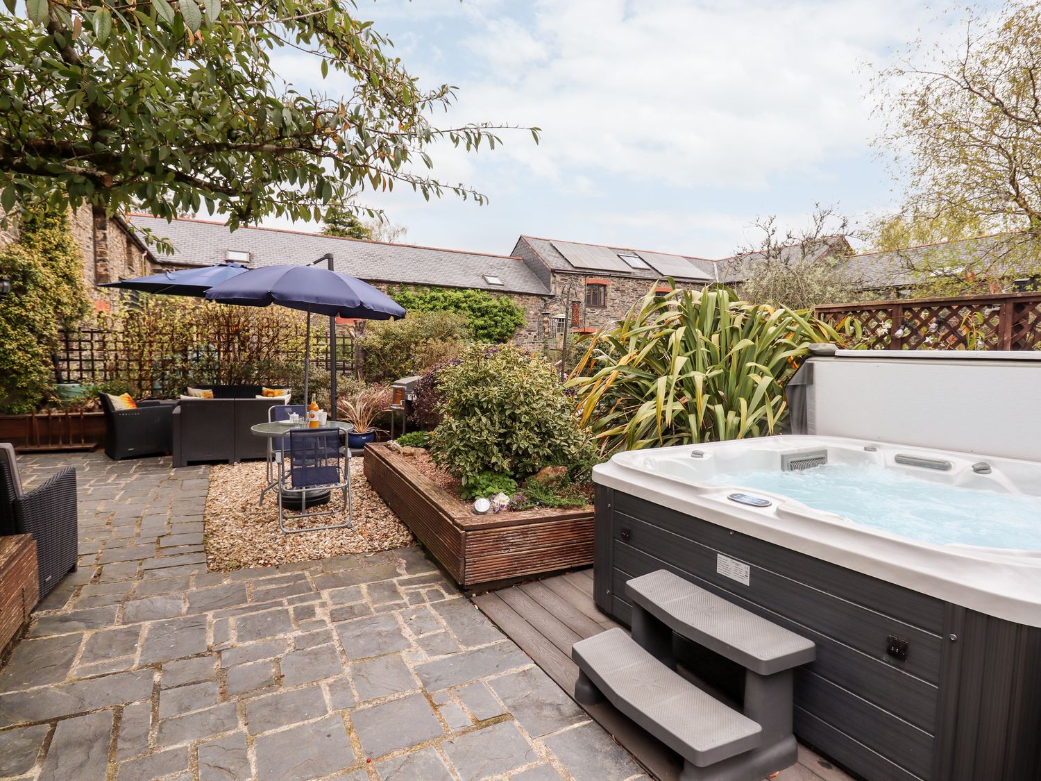An outdoor patio with a hot tub small table with umbrella and seating area at Foxglove Barn South Brent
