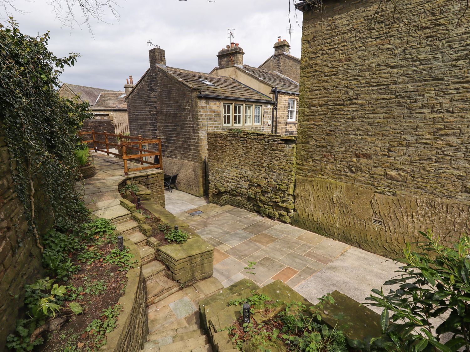A stone paved courtyard with stone steps and walls surrounded by old stone buildings at Erin Cottage in Haworth