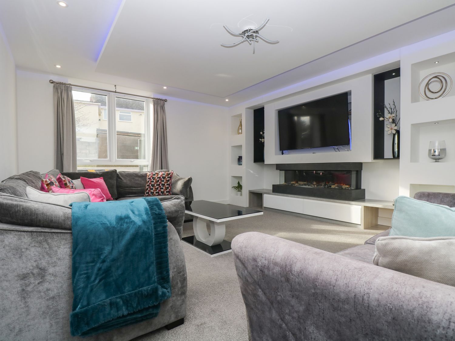 A living room with sofas pillows a coffee table a wall-mounted TV and a fireplace at Llawnroc in Mullion