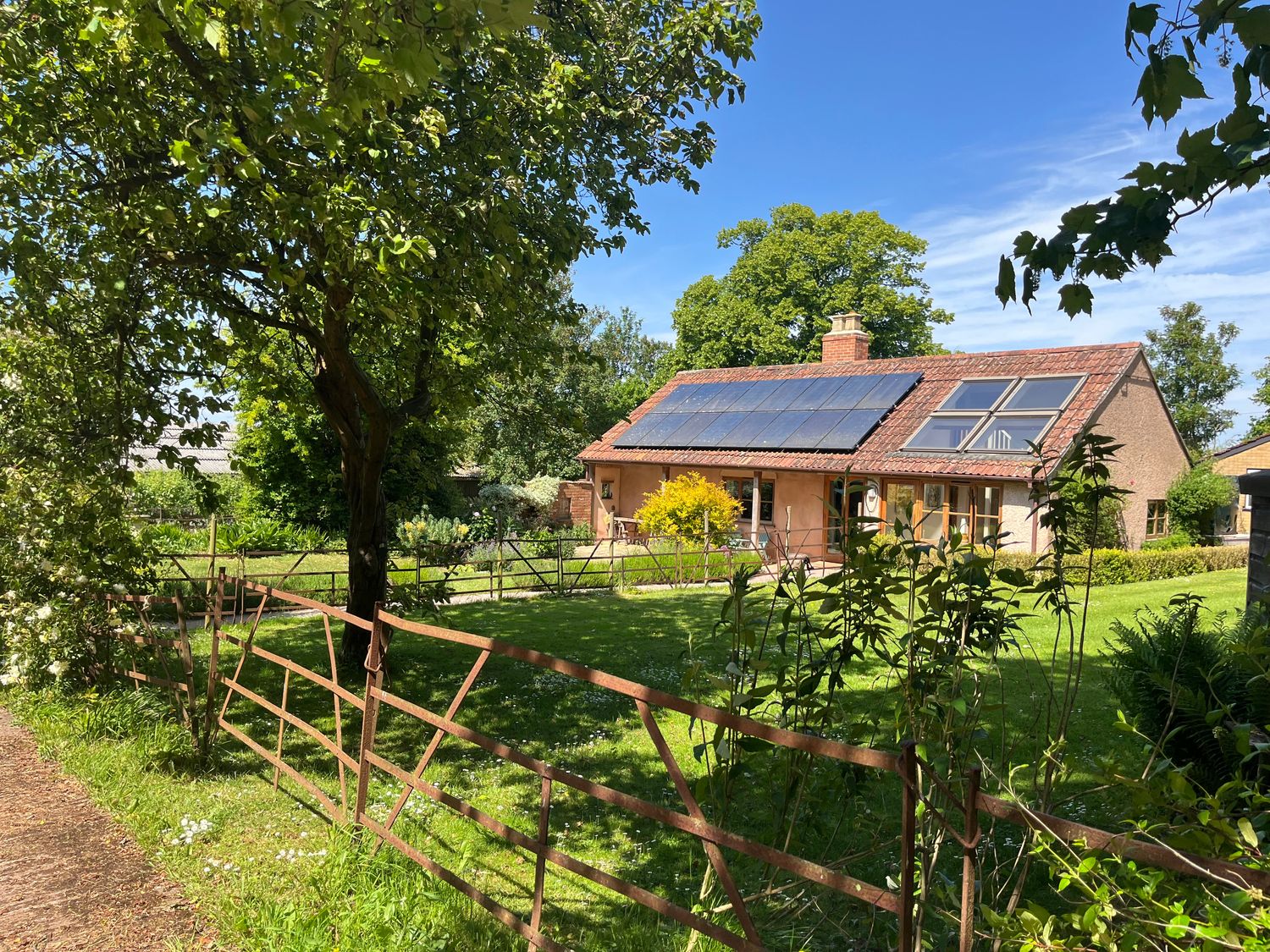 A house with solar panels on the roof behind a metal fence and trees at The Apple House in Spaxton near Nether Stowey