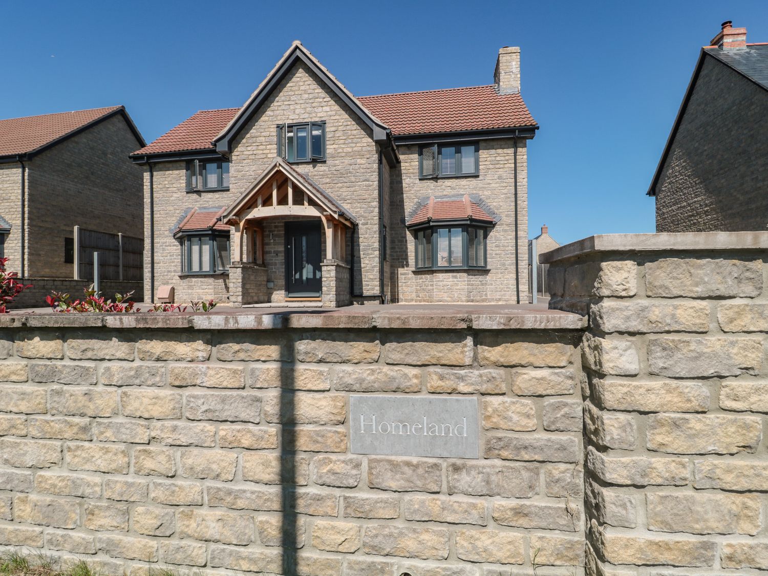 A stone house with a tiled roof behind a stone wall with a Homeland sign in Somerton