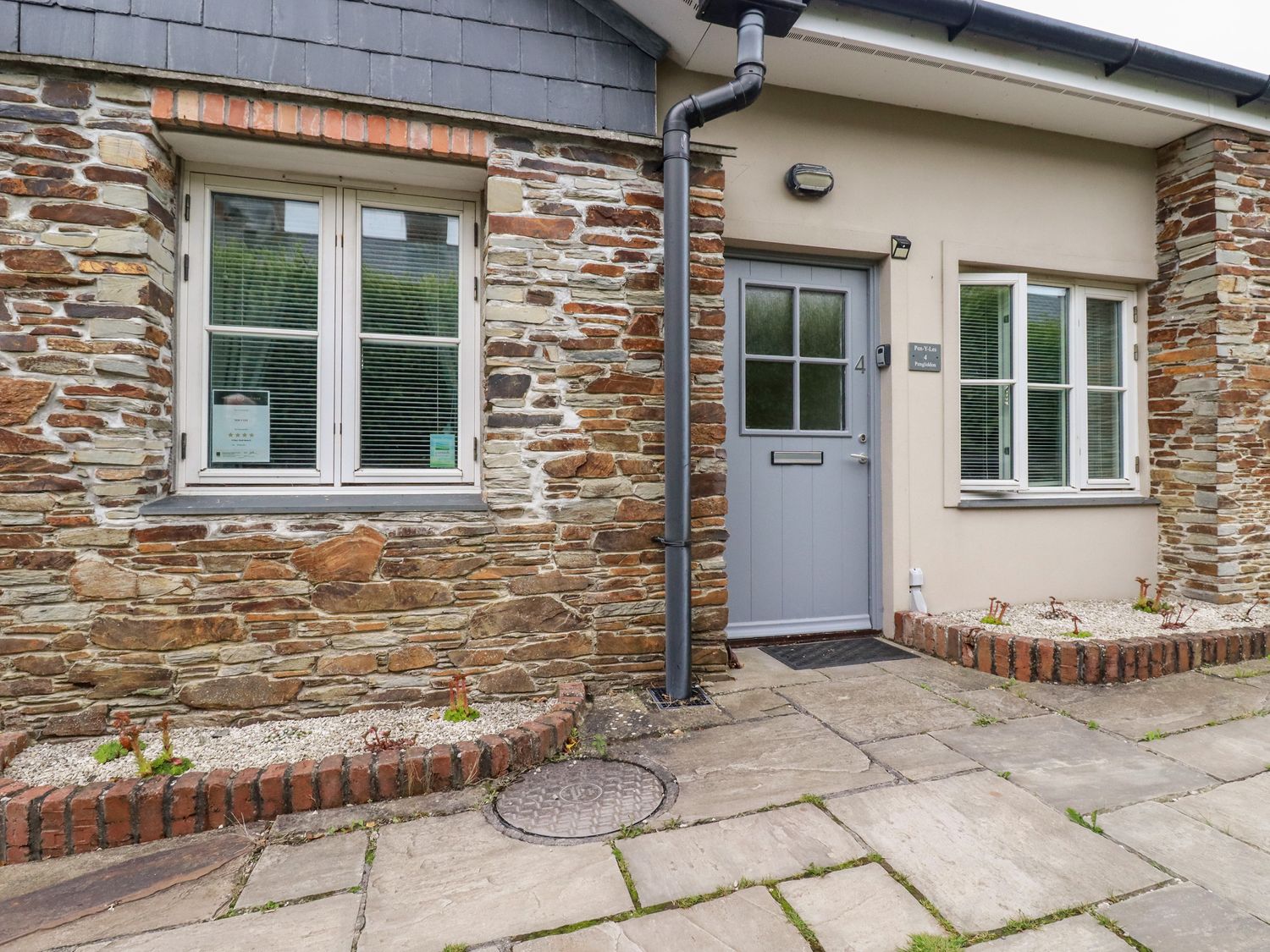 The entrance of a stone and brick house with two windows and a gray door with the number 4 at Pen-Y-Les in Wadebridge