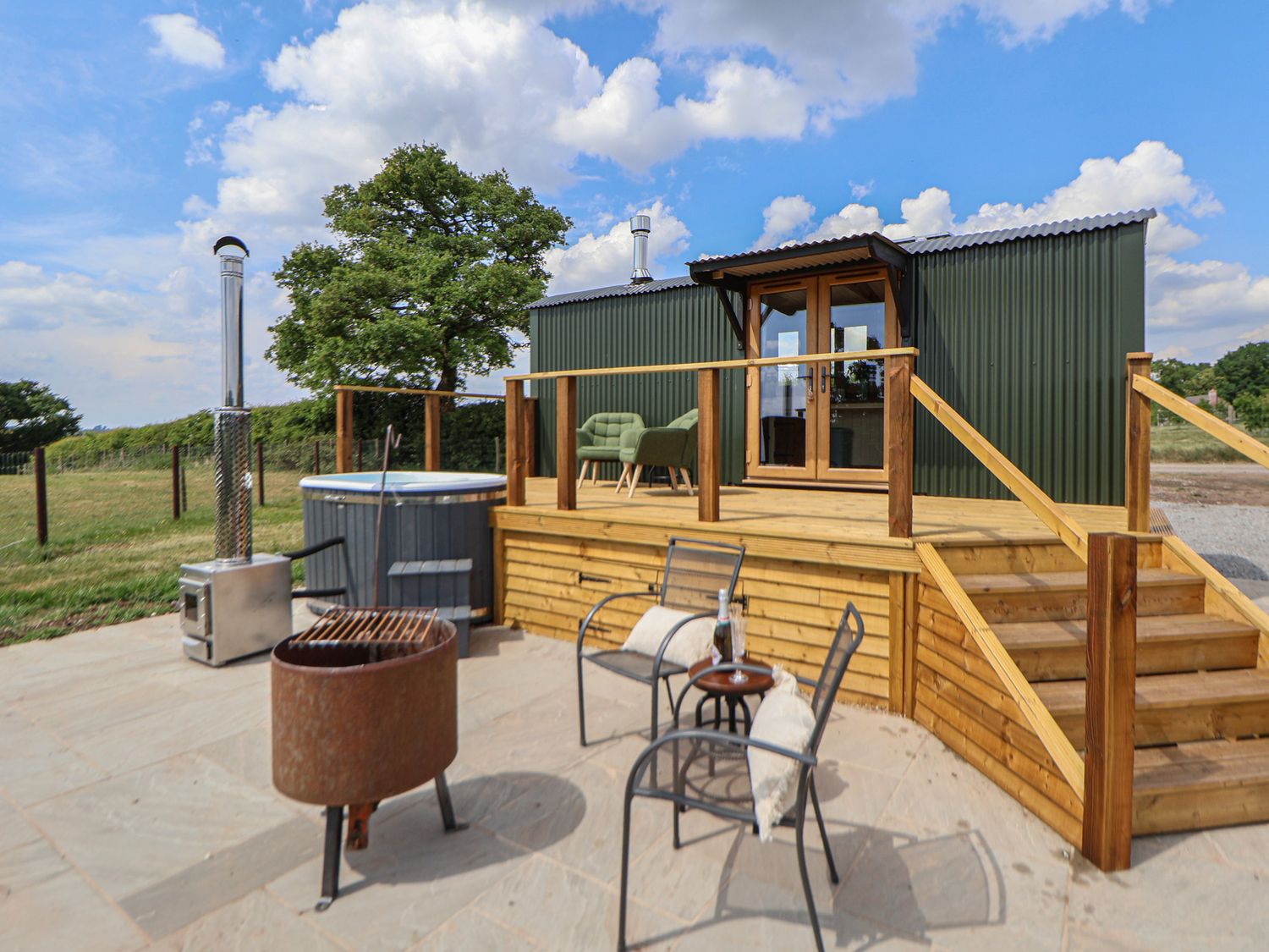 An outdoor patio with chairs a fire pit hot tub and a wooden deck at The Coop in Aston near Woore