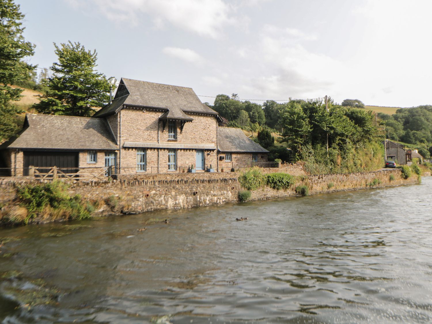A stone house beside a river with greenery and trees in the background at Bridgend Barn in Newton Ferrers