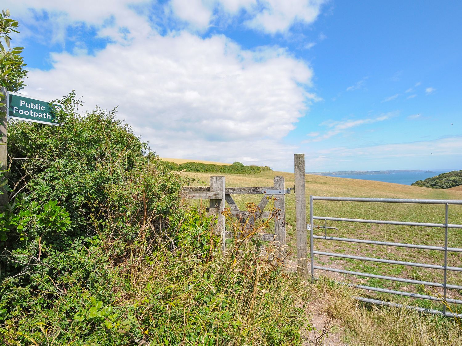 A countryside footpath gate next to a metal gate with a view of fields and the sea at Midway Lodge in Cawsand near Kingsand