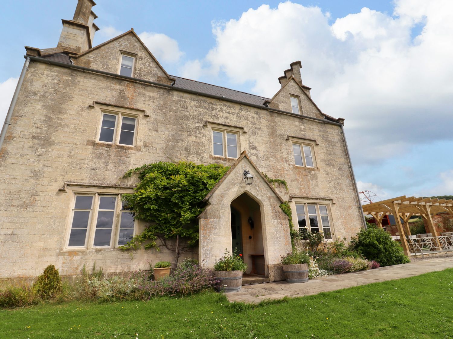 A stone building with an arched entrance and windows surrounded by grass and plants with a covered outdoor seating area at Hammonds Farmhouse in Stroud