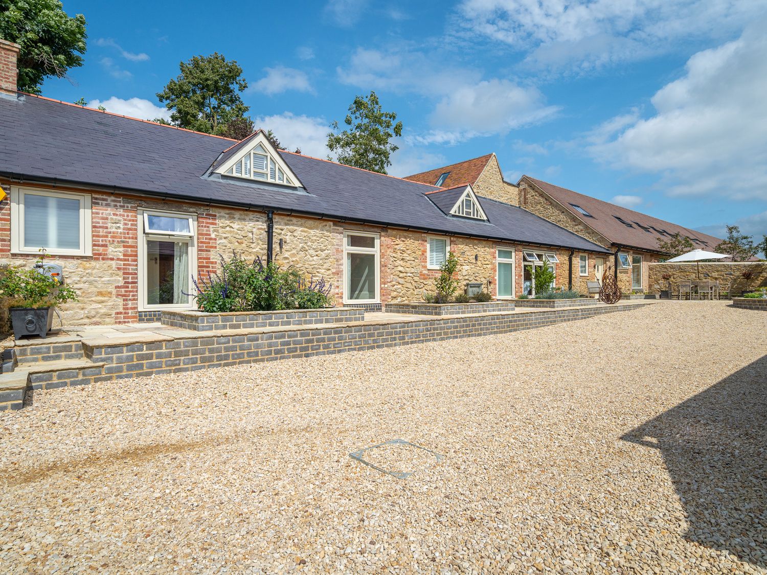 A stone building with multiple windows and a gravel courtyard at The Stables in Wheatley