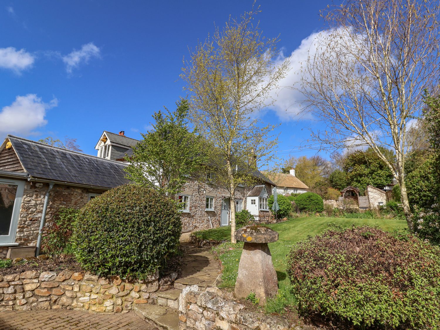 A stone cottage with a garden and trees at Bridge Cottage in Dalwood