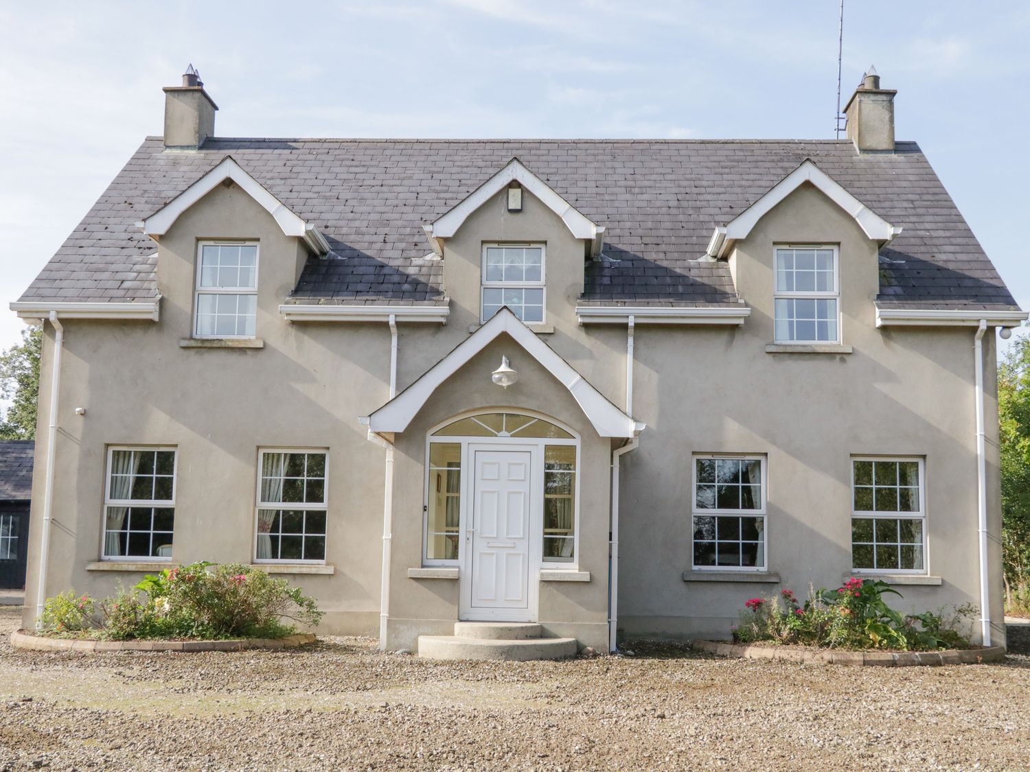 A two story house with a central white door and five windows a gravel driveway and small garden beds in front at Craiglea Cottage in Killeague near Coleraine