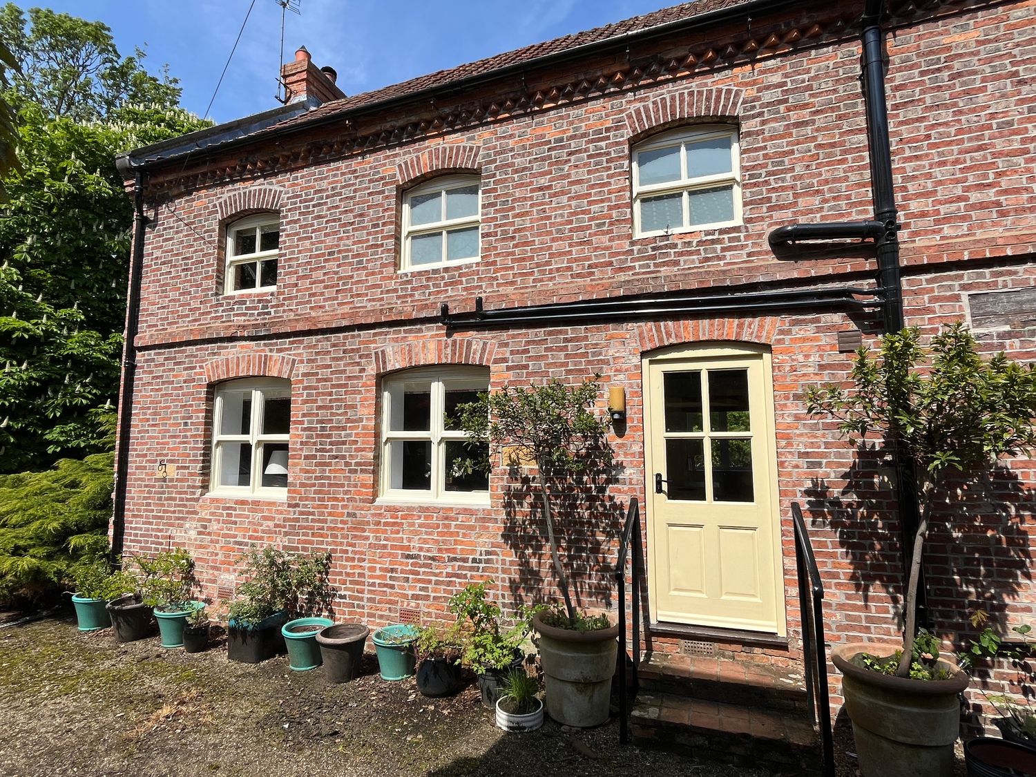 A brick exterior wall with multiple windows a cream door and several potted plants outside at The Old Barn in Caenby