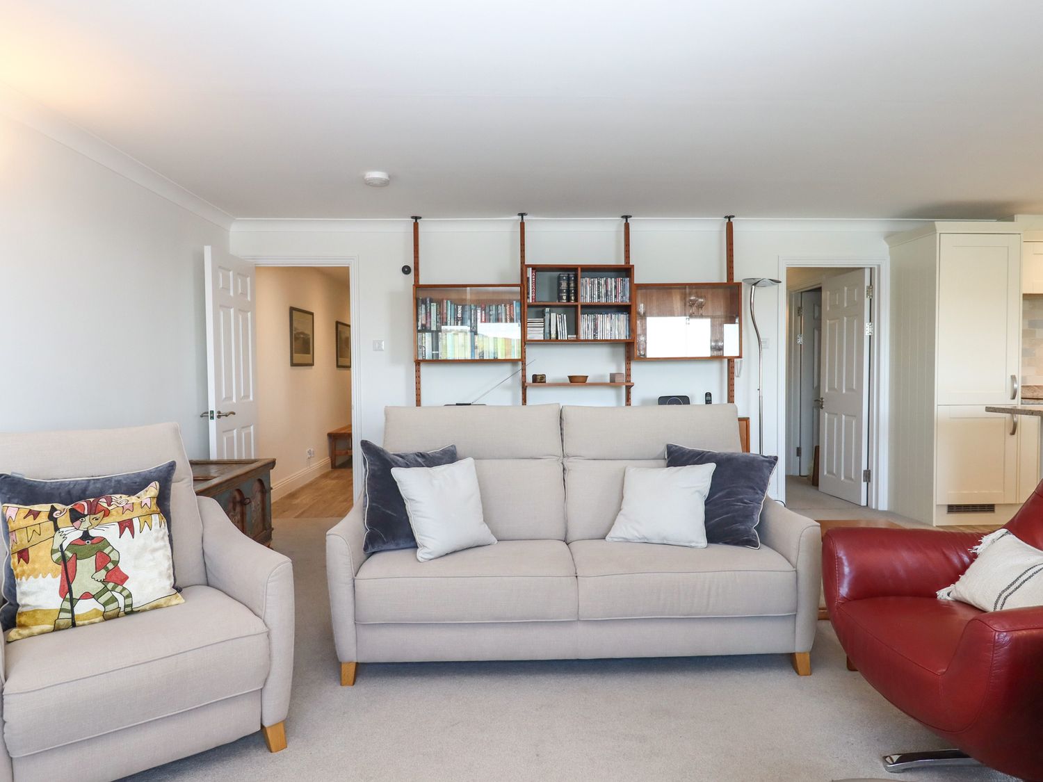 A living room with beige sofas and a red armchair with a shelving unit on the wall at 14 Burgh Island Causeway in Bigbury-On-Sea