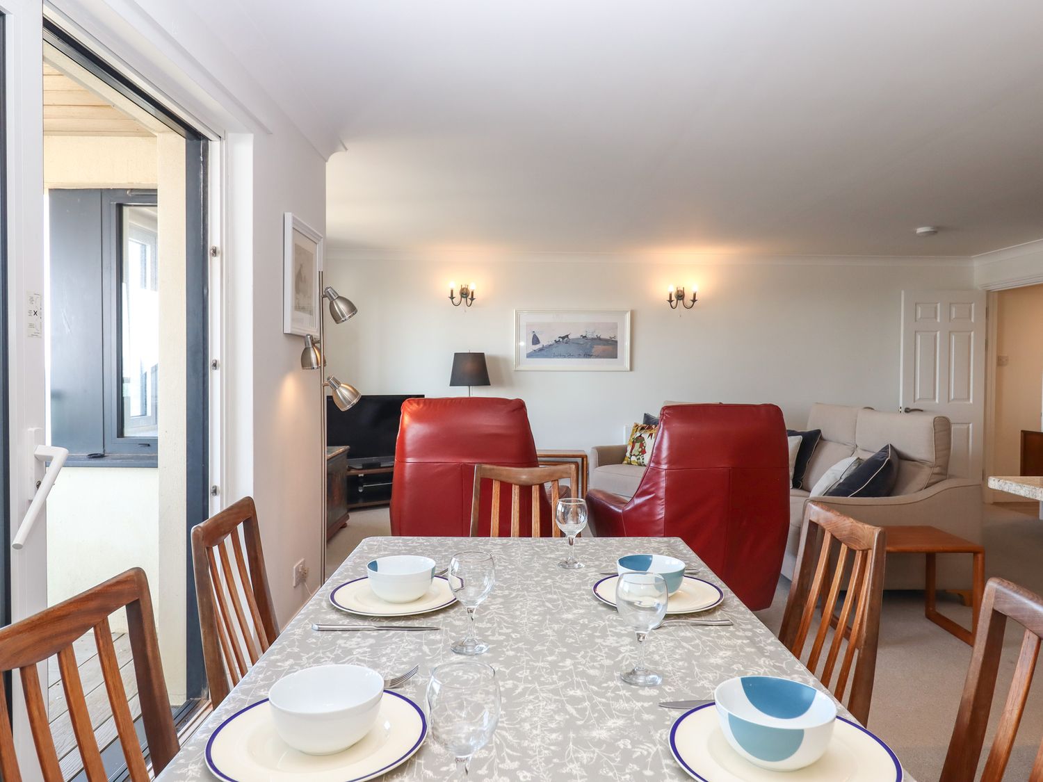 A dining table set with plates and bowls in an open living and dining room with red armchairs and a beige sofa at 14 Burgh Island Causeway in Bigbury-On-Sea