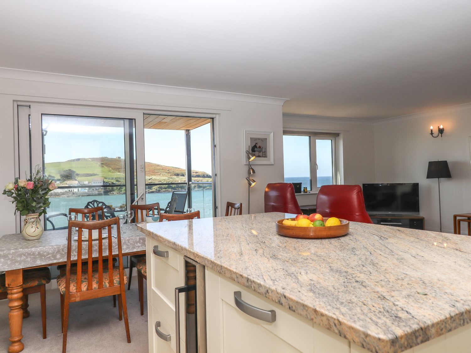 A dining area with wooden chairs and a table next to large sliding glass doors with water and hills outside at 14 Burgh Island Causeway in Bigbury-On-Sea