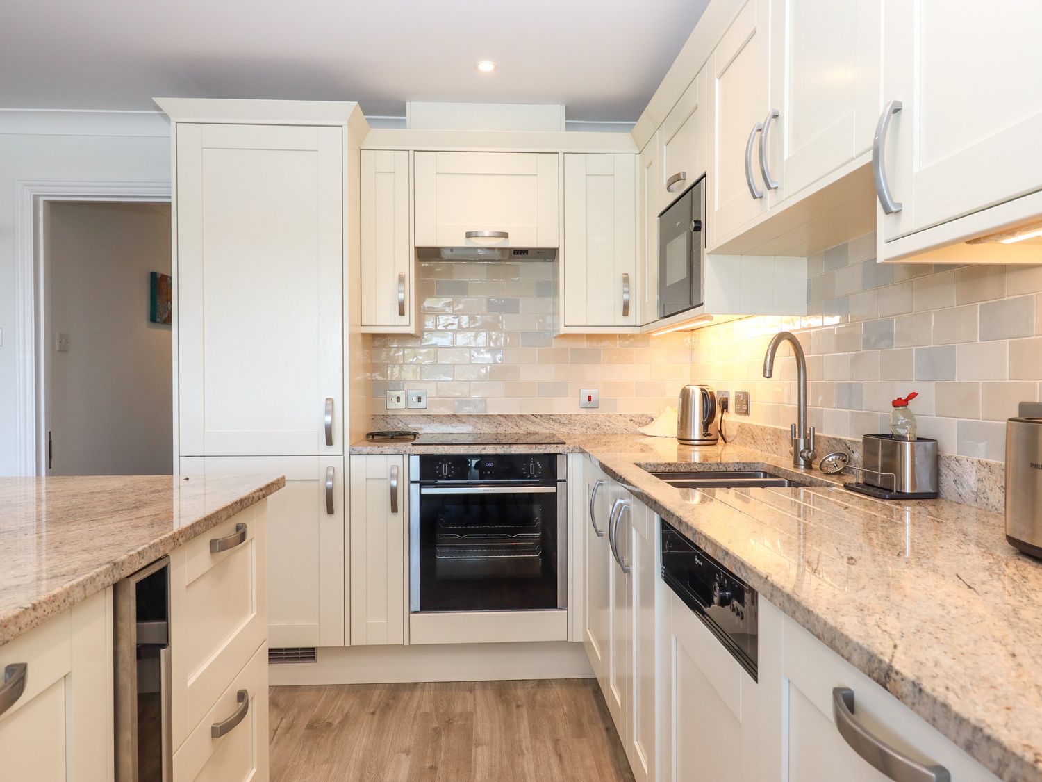 A kitchen with white cabinets granite countertops oven dishwasher microwave kettle and wooden floor at 14 Burgh Island Causeway Bigbury-On-Sea