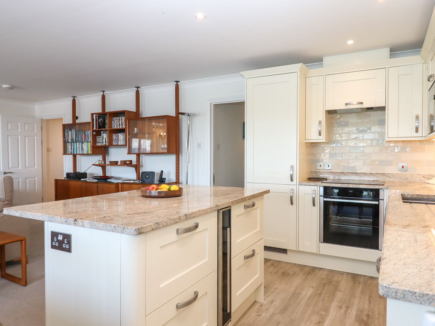 A kitchen with cream cabinets and a granite countertop island with a fruit bowl at 14 Burgh Island Causeway in Bigbury-On-Sea