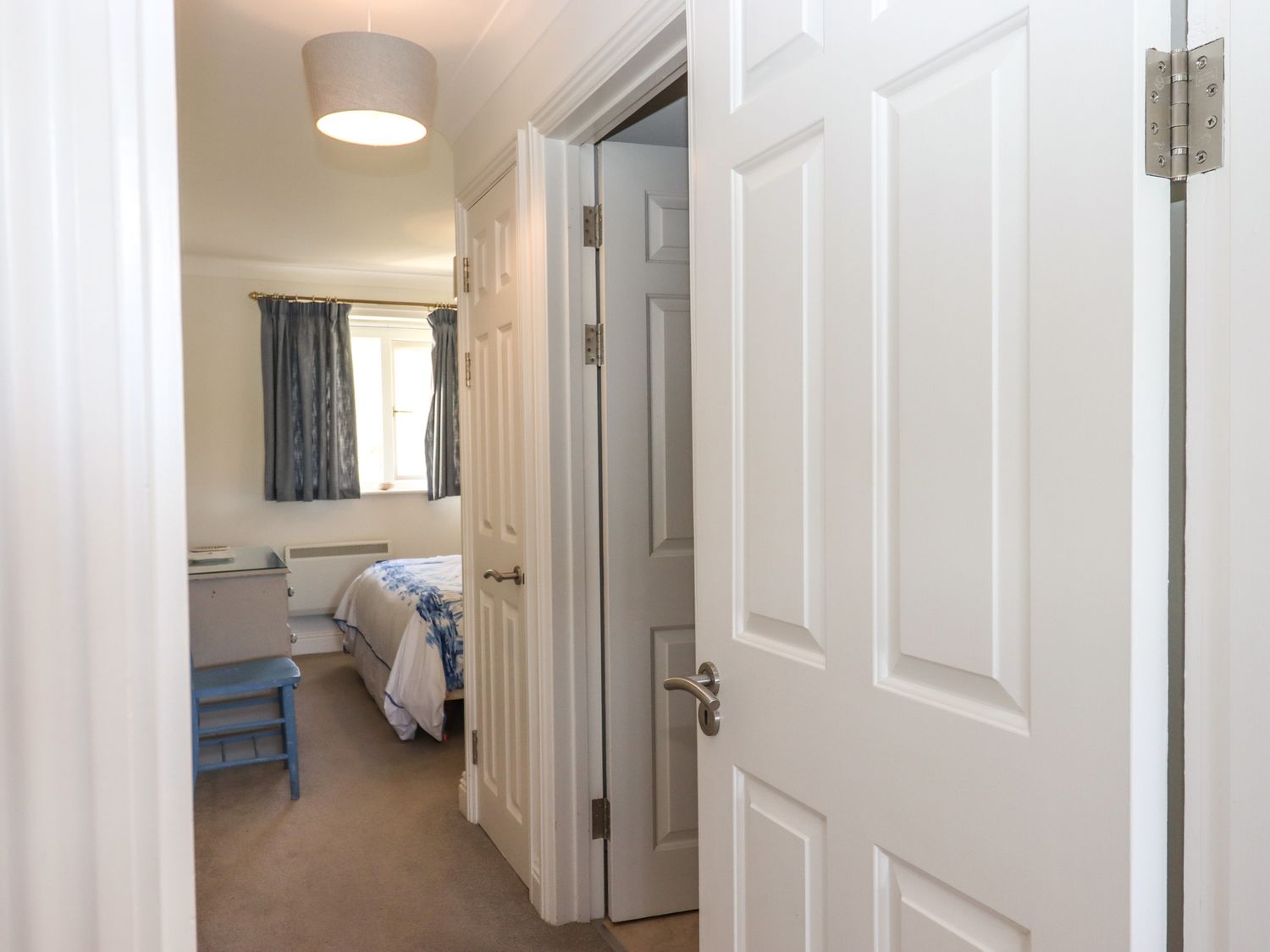 A hallway with open white doors leading to a bedroom with a bed and blue curtains at 14 Burgh Island Causeway in Bigbury-On-Sea