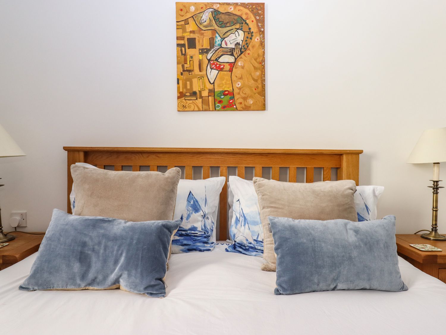 A bed with wooden headboard and several pillows in a bedroom with a painting above the headboard at 14 Burgh Island Causeway in Bigbury-On-Sea