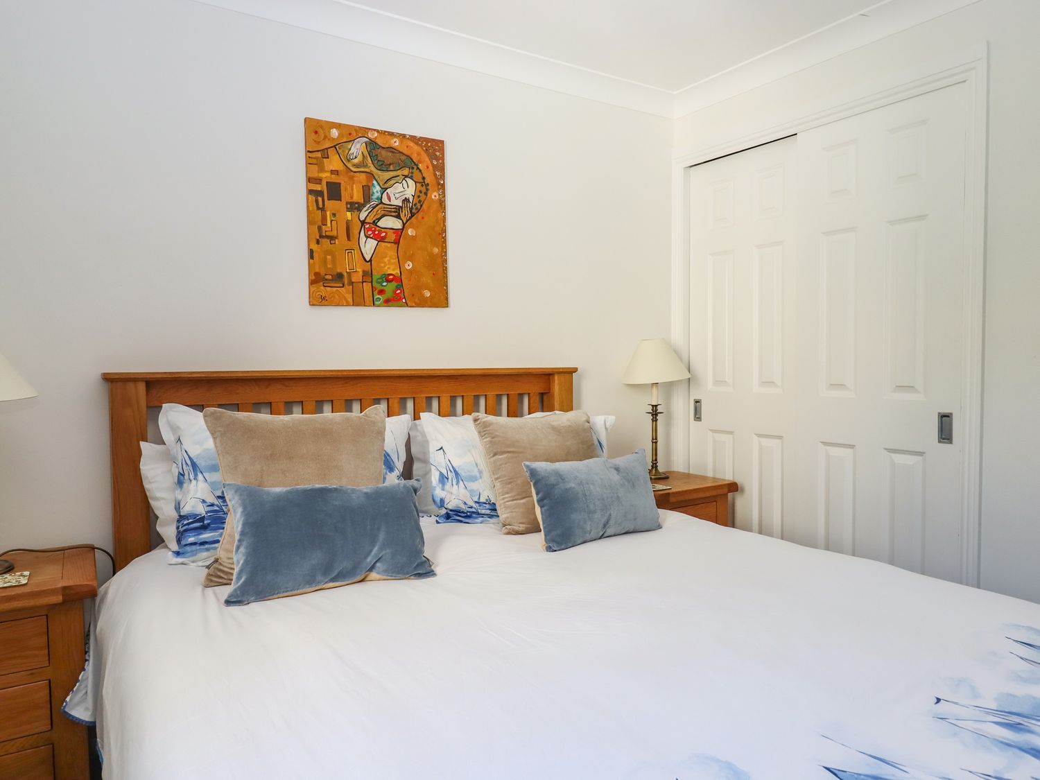 A bedroom with a wooden bed frame white bedding decorative pillows wooden nightstands with lamps and a painting on the wall at 14 Burgh Island Causeway in Bigbury-On-Sea